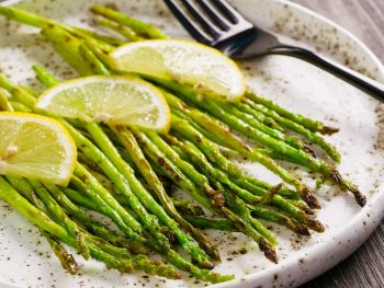 Tasty grilled asparagus on white platter garnished with lemon slices on top