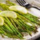 Tasty grilled asparagus on white platter garnished with lemon slices on top