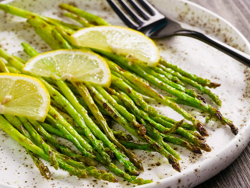 Tasty grilled asparagus on white platter garnished with lemon slices on top
