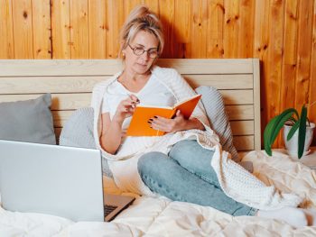 Woman writes in her journal as she lays in bed after hysterectomy.