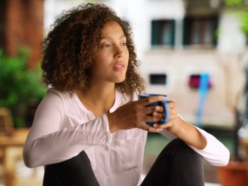 Woman sipping a cup of coffee and thinking outside her home after recovering from hysterectomy surgery.