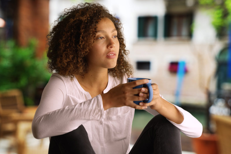 Woman sipping a cup of coffee and thinking outside her home after recovering from hysterectomy surgery.
