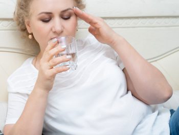 Woman drinks water as she tries to cool down from a hot flash