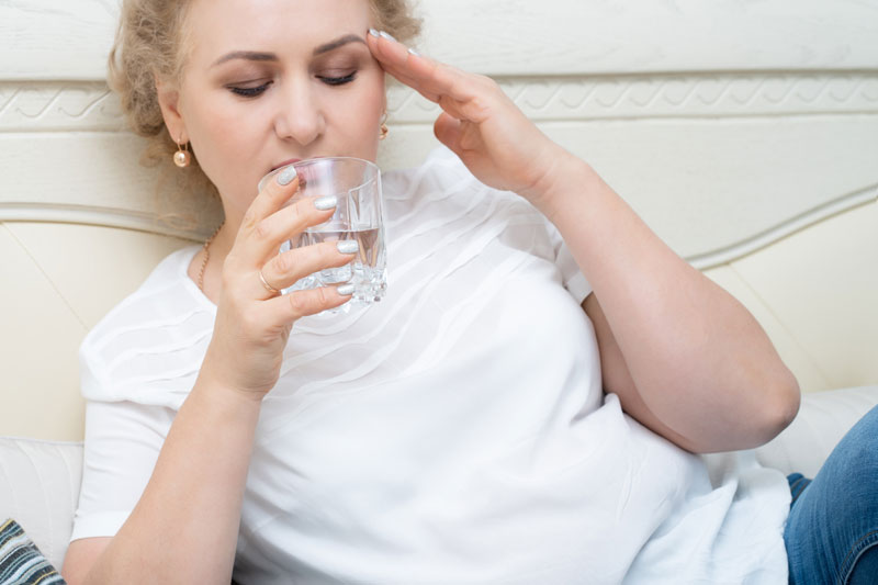 Woman drinks water as she tries to cool down from a hot flash